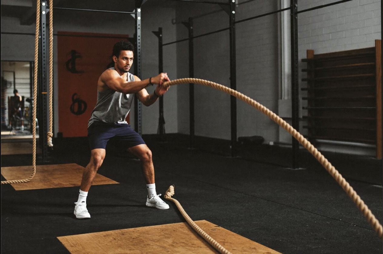 Man training with battle ropes in the gym, a conditioning session that builds strength and aerobic fitness together