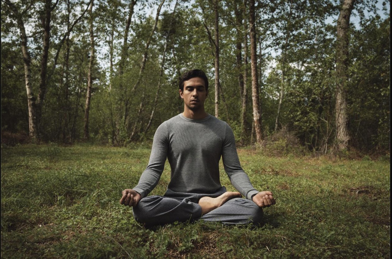 Man meditating cross-legged in a forest clearing, taking time to manage stress between training sessions