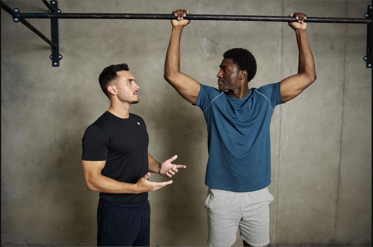 Coach counting reps with an athlete during a pull-up set, building a track record of small wins