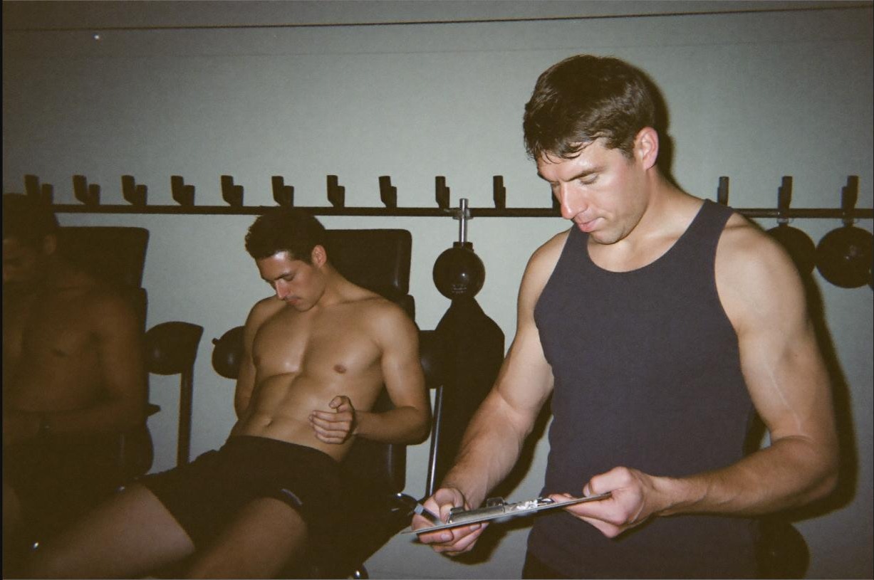 Coach observing a client's training session with a clipboard, monitoring for early signs of overtraining